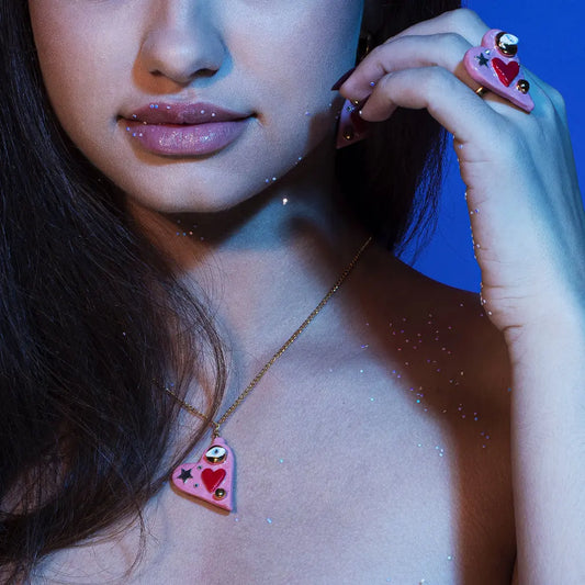 A close-up of a woman wearing the All You Need Is Love necklace, featuring a hand-made ceramic heart pendant, 24K gold lustre, a gold-over silver star, and a Swarovski crystal.