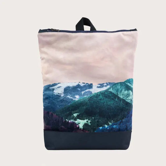 A minimalist BLUE MOUNTAINS backpack featuring a mountain range design. Velvet top, navy blue bottom, adjustable straps, laptop pocket, and zip closure. Dimensions: 44cm height, 36cm width.
