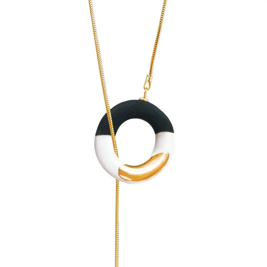Handmade ceramic Big OM Choker necklace in black and white with 24K gold details. Features a circular pendant on a gold-over-silver chain. Length approximately 80 cm. Unique variations possible.