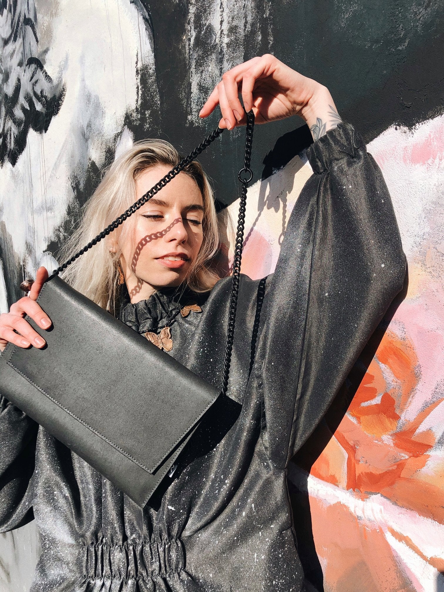 A woman elegantly holds a black leather shoulder bag with a chain strap. Crafted from premium genuine leather, featuring a flap front and magnetic closure for style and functionality.