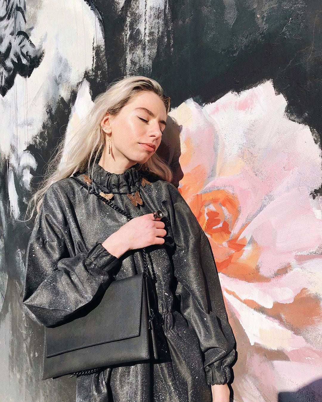 A woman poses with a Classic Black Matte Leather Shoulder Bag, showcasing its sleek design and chain strap. Crafted from premium genuine leather, this handcrafted bag exudes timeless elegance and practicality.