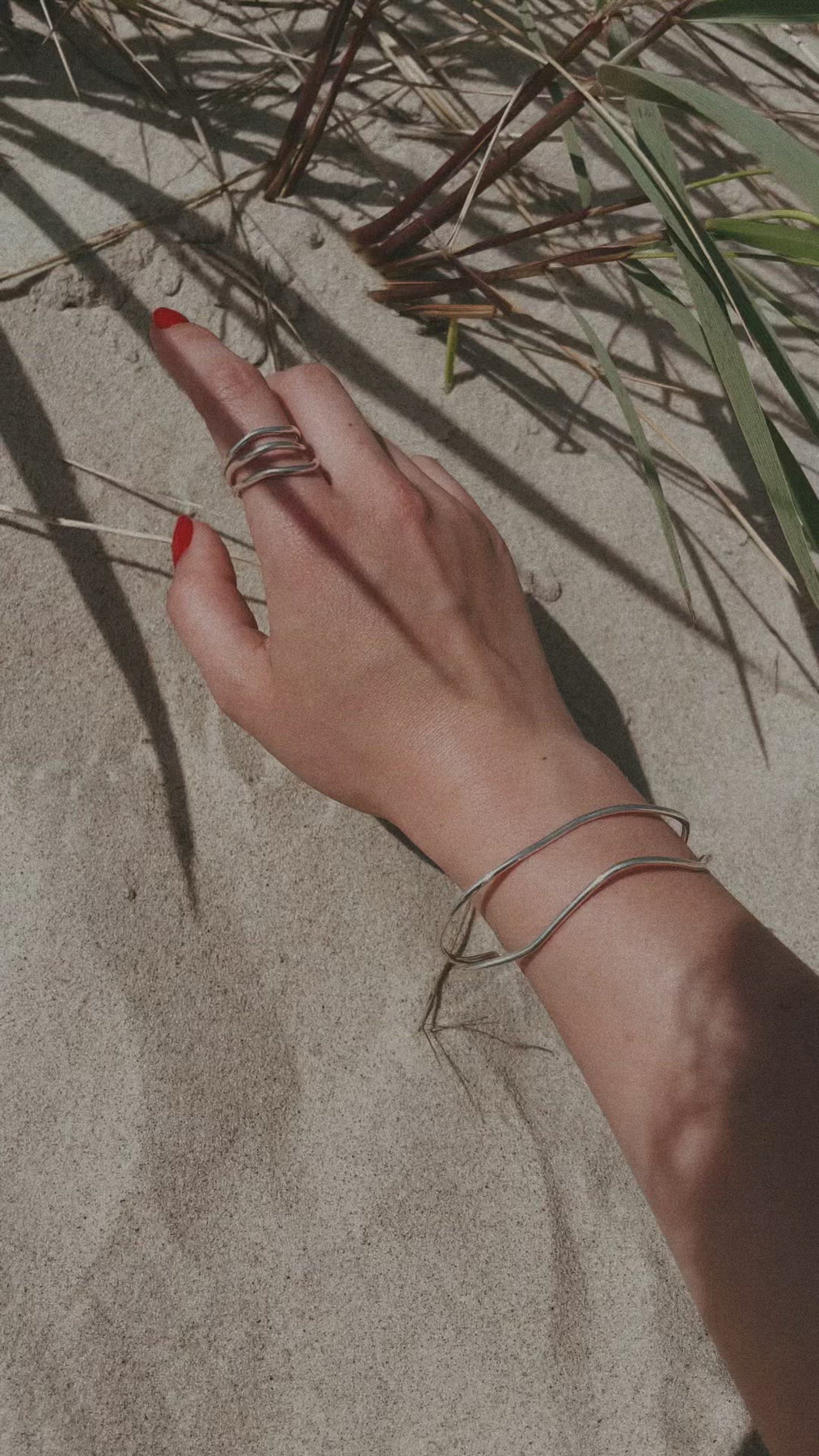 A hand with silver bracelets on sand, showcasing Double Ring - Silver. Hand-crafted from sustainable sterling silver, two 3mm rings stacked for a versatile look. Warranty included.