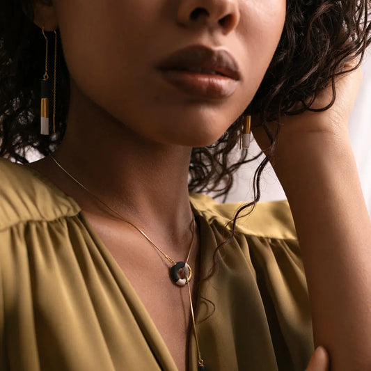 A woman wearing a gold OM Choker necklace and earrings, embodying the Circle of Life concept with a hand-made ceramic pendant and 24K gold details.