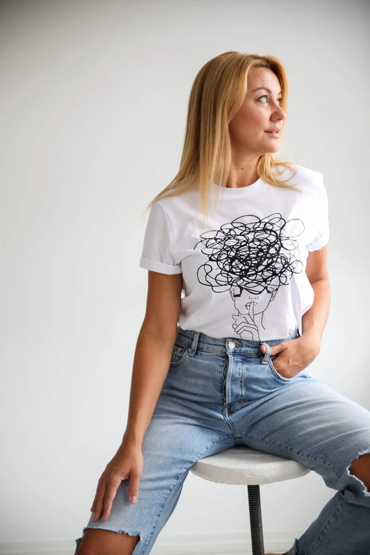A woman in an oversized Ssshhh! T-shirt, sitting on a chair. Product details: XS to XL sizes, white shirt with a drawing. Size chart: Width - 47 to 59 cm, Length - 68 to 76 cm. Washing instructions included.