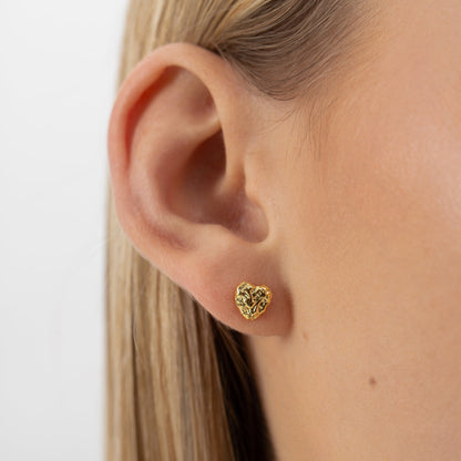 Close-up of a woman's ear wearing a gold heart-shaped stud earring. Hypoallergenic, sustainable, 18k gold plated, 925 sterling silver. Elegant, minimalist accessory for all occasions.