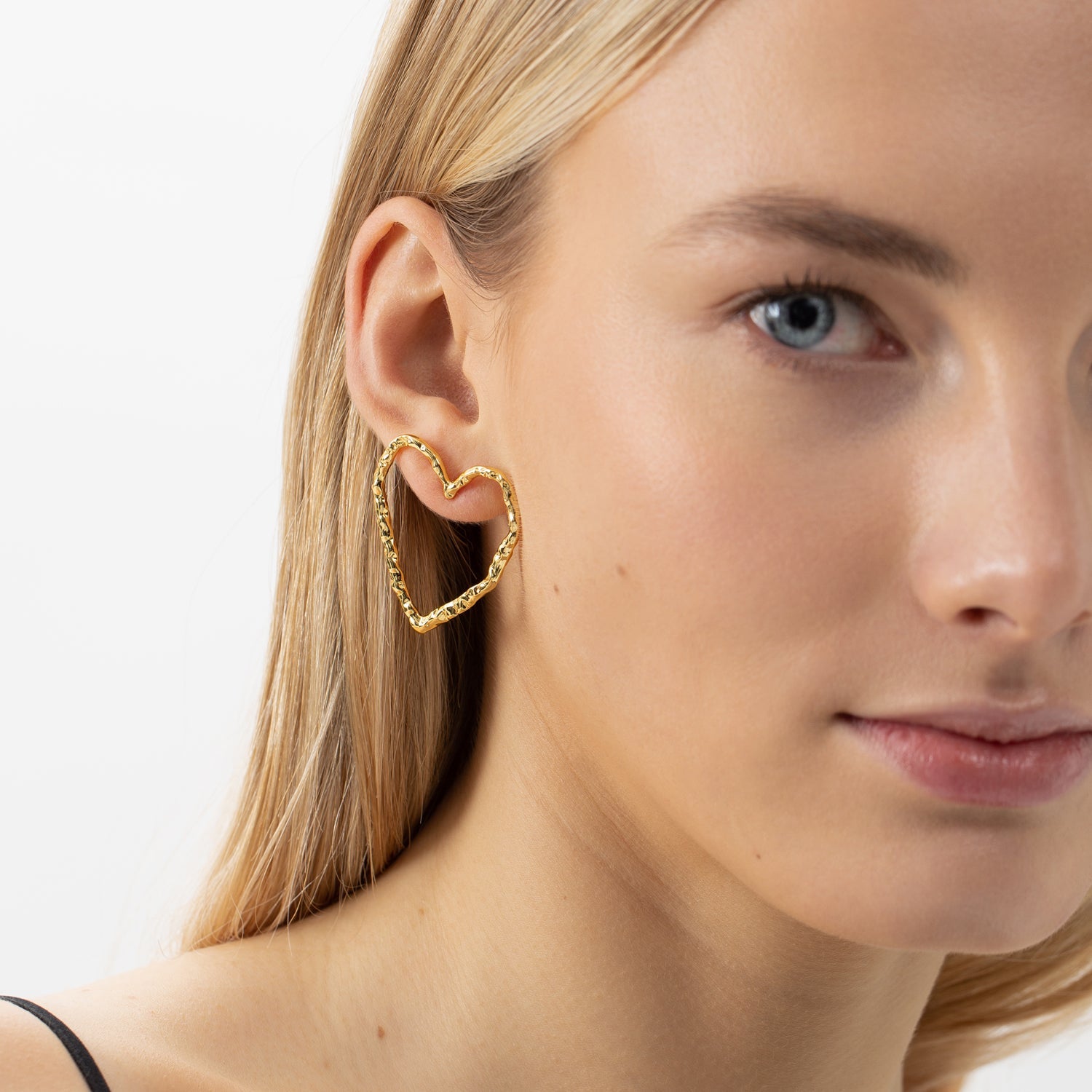 Stud Earrings EROS - Gold: Close-up of a woman wearing heart-shaped silver earrings, hypoallergenic and sustainable, made from recycled materials.