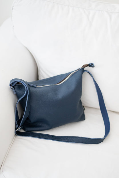 Handmade Anet L shoulder bag crafted from blue leather, resting on a white couch. Each bag is unique, made from furniture industry leftovers in Estonia.
