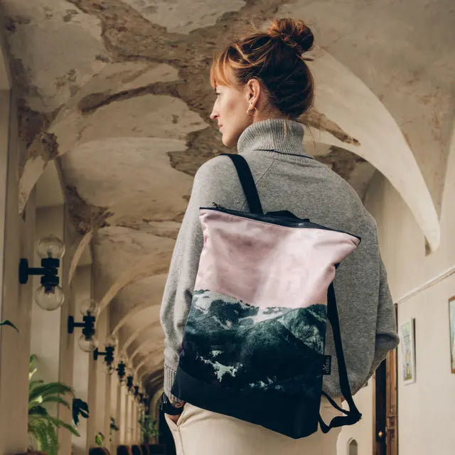 A woman in a grey turtleneck sweater with a pink and black Blue Mountains backpack. Stylish and practical, perfect for everyday use.