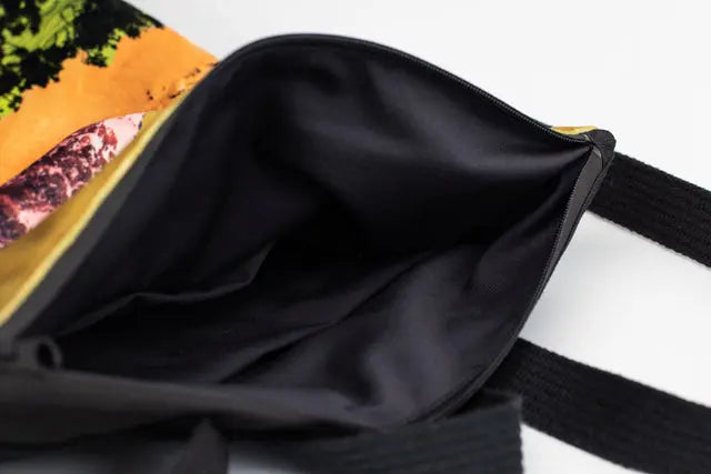 A close-up of a black backpack with a colorful fabric interior, featuring a design of Mountains. Spacious, lightweight, with adjustable straps, zipper closure, and pockets for a 13 laptop.