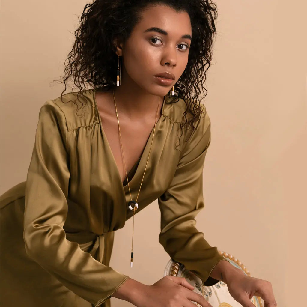 A woman in a green dress with curly hair wearing a gold necklace, showcasing the Big OM Choker Black and White pendant on a 24K gold-over 925 sterling silver chain.