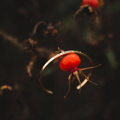 A gold ring delicately placed on a rosehip, symbolizing the bracelet Live Laugh Love - a reminder of laughter and love in life. Durable stainless steel, adjustable design.