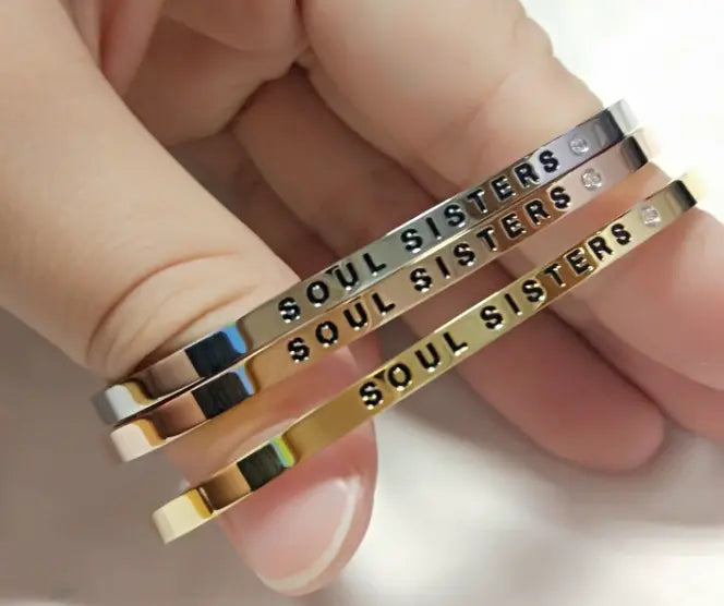 A hand holding a stack of bracelets, showcasing the adjustable and durable Soul Sisters bracelet. Engraved with a heartfelt message, this stainless steel piece is a meaningful gift for cherished ones.