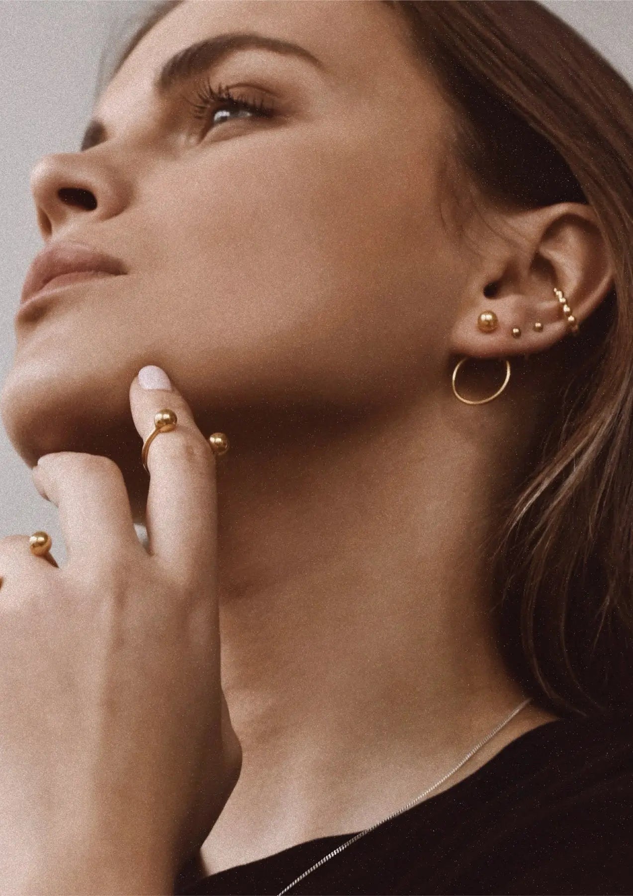 A woman with her eyes closed wearing Chord Earrings - Gold, featuring a front-facing ball design and circle at the back. Hand-made with 24k gold plating on sterling silver.