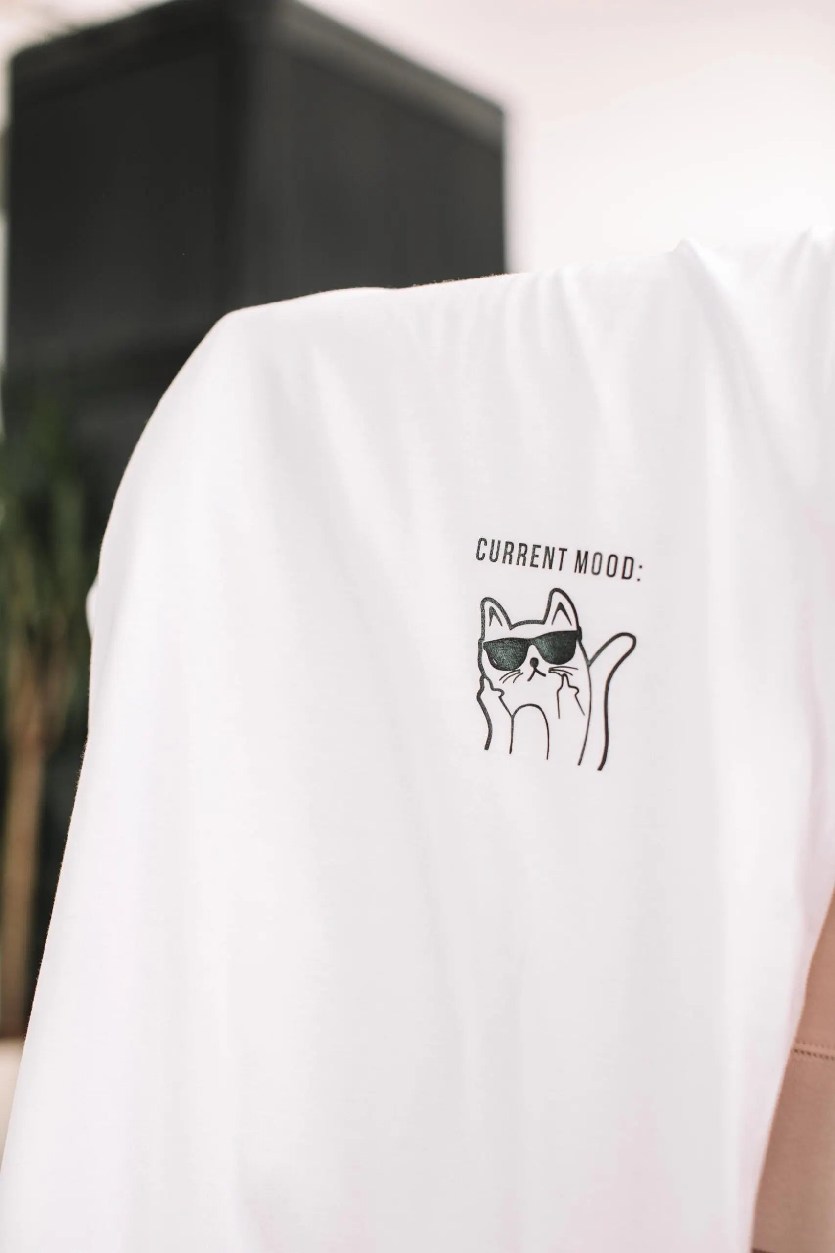 An oversized white organic cotton t-shirt featuring a printed 'Current Mood' design with a cat. Size chart: XS - XL. Washing instructions included.