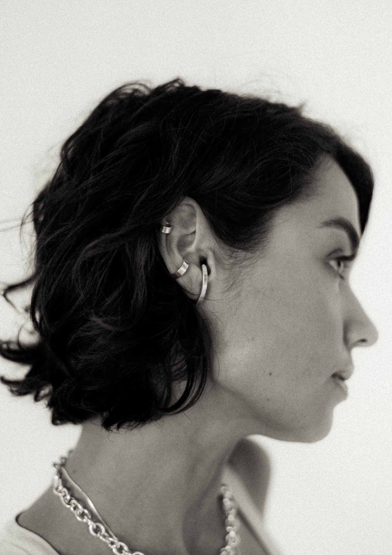 A woman wearing a Flat Ear Cuff in Silver, a sleek non-piercing accessory. Handmade from sterling silver, 4mm wide, 0.84mm thick, weighing 1.05g. Sustainable packaging included.