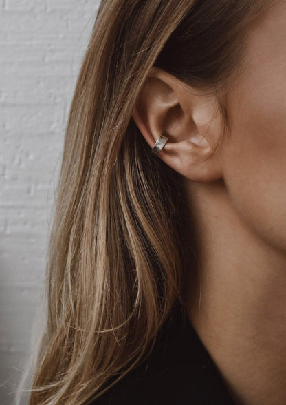 A detailed close-up of a woman's ear showcasing the Flat Ear Cuff in Sterling silver by NO MORE, a comfortable, non-piercing accessory handcrafted sustainably in Lithuania.