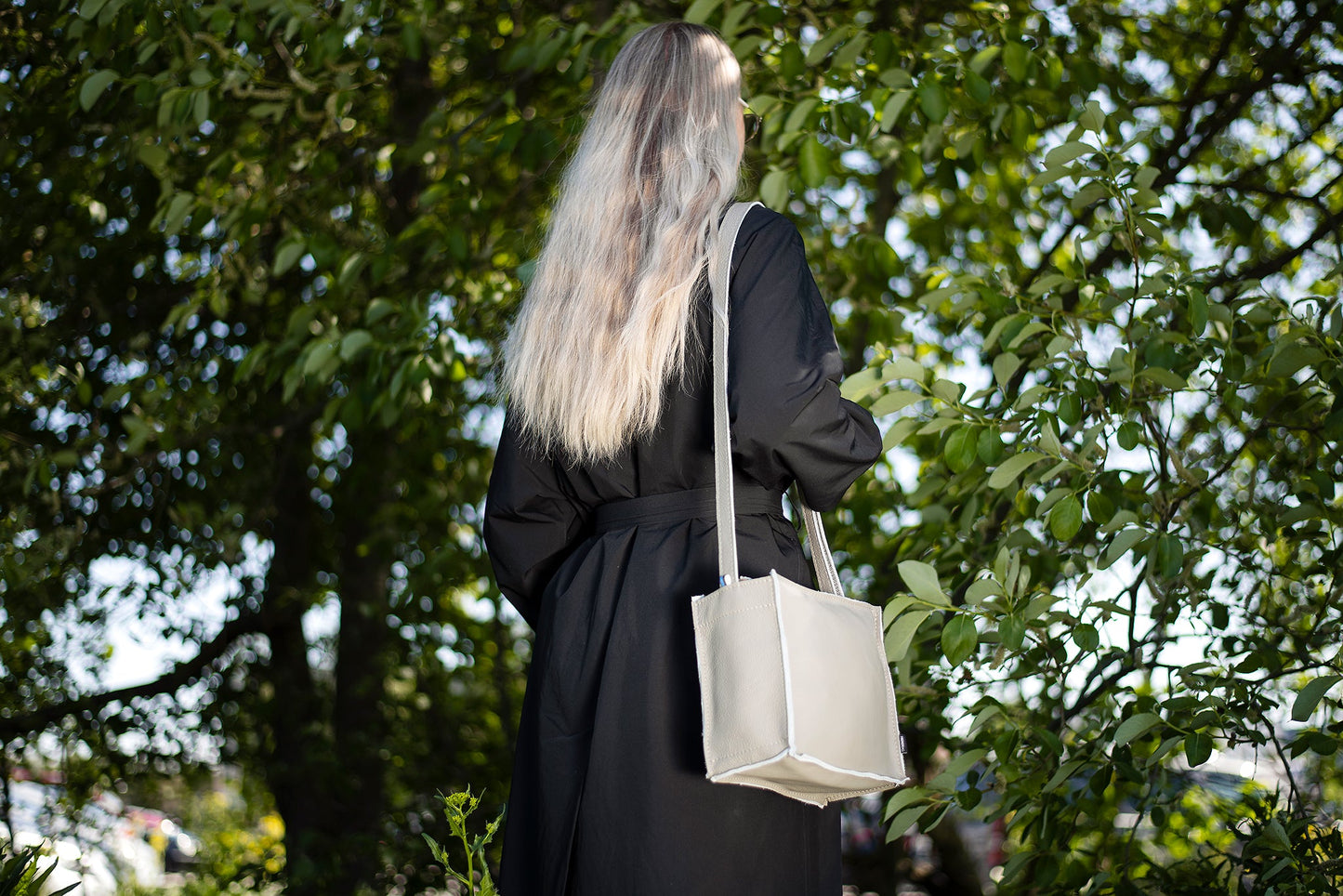 Handmade Folk 1 shoulder bag from furniture industry leftovers. Unique design, eco-friendly, durable. Made in Estonia. Woman in black coat with white purse outdoors.