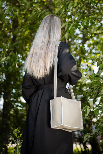 A woman with long hair carries the Folk 1 shoulder bag, made from furniture industry leftovers, showcasing eco-friendly and durable design. Handcrafted in Estonia.