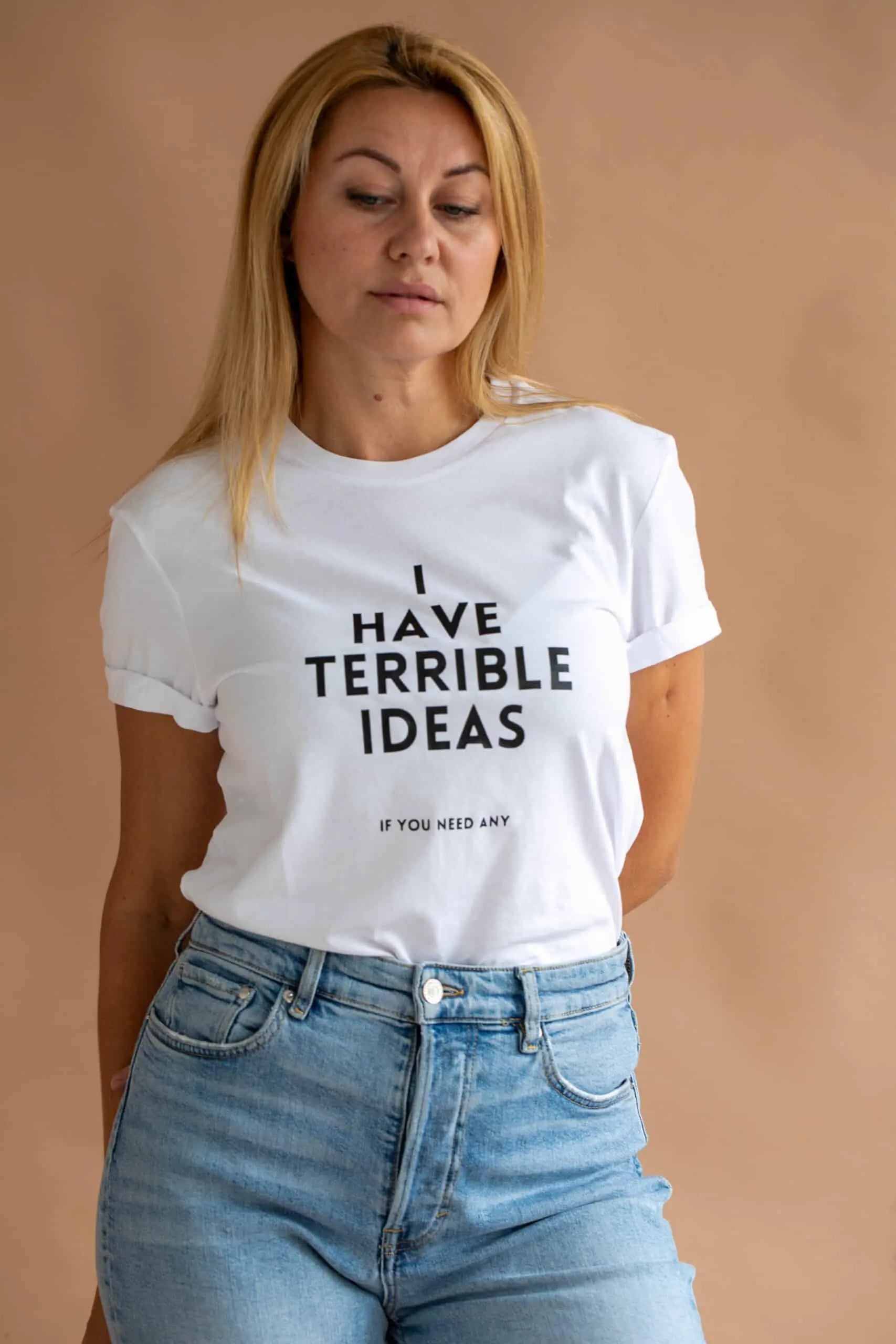 A woman in an oversized white t-shirt with black text I Have Terrible Ideas, paired with blue jeans, posing for a photo. Casual and humorous organic cotton tee.