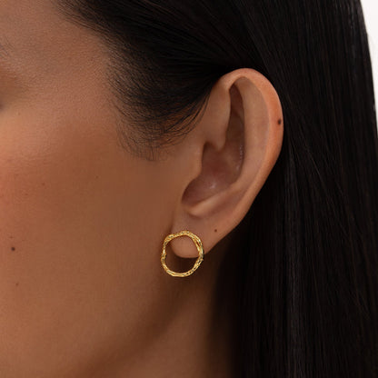 Close-up of a woman's ear wearing minimalist circle-shaped Echo golden stud earrings made of 925 sterling silver, 18k gold plated, hypoallergenic, and sustainable.