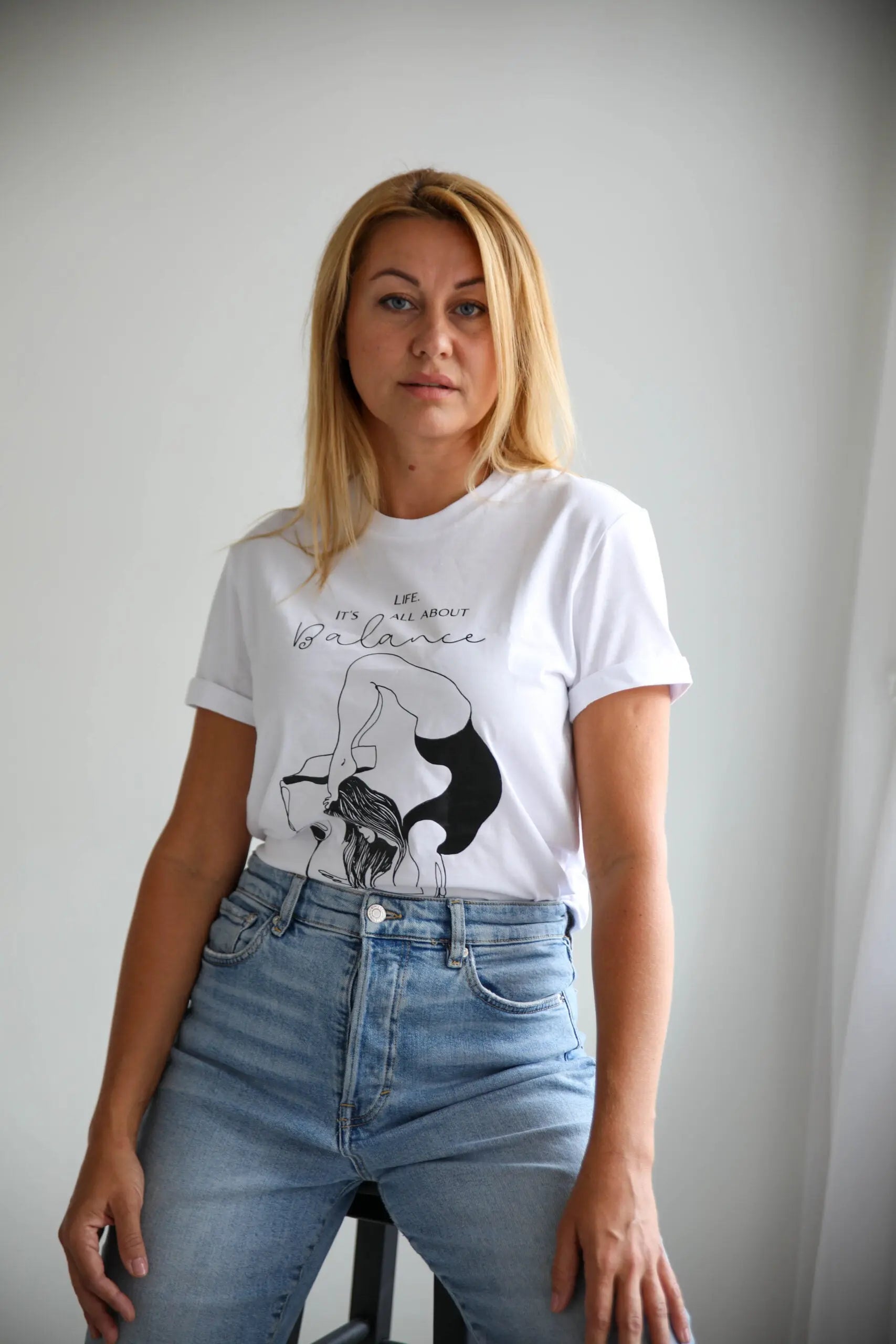 A woman in an oversized white t-shirt with a graphic print 'Life. It's all about balance'. Product emphasizes organic cotton, oversized fit, and washing instructions.