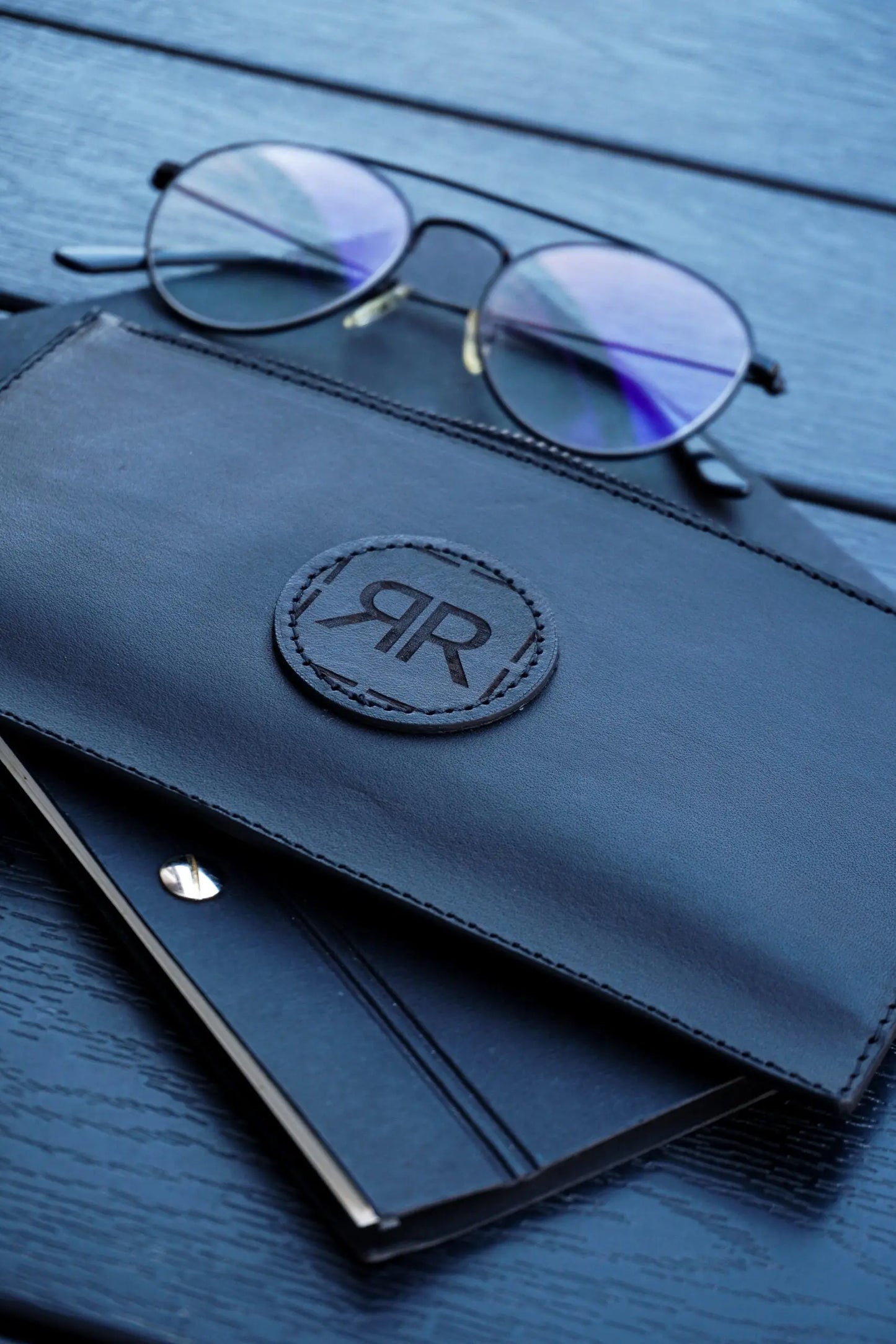 A black leather wallet with a logo and glasses on a table, showcasing a sleek design with a removable wristlet for convenience and elegance.