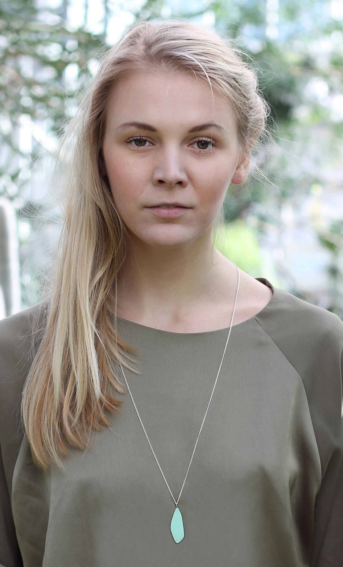 A woman with long blonde hair wearing the Leaves Small necklace by Lisa Kroeber Jewellery. Handmade in Europe, featuring a powder-coated brass and silver pendant on an 85 cm chain.