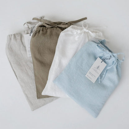 A group of linen Primrose loungewear set bags with tags, showcasing a relaxed fit shirt and trousers. Handmade from 100% linen, OEKO-TEX certified, packaged in a matching linen bag.