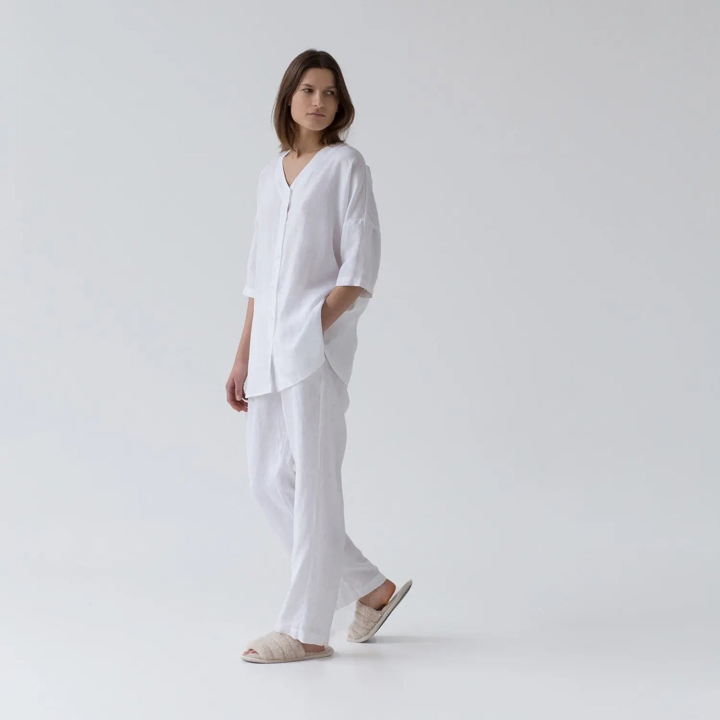 A woman in white linen Primrose loungewear set, featuring a V-neck shirt and relaxed-fit trousers with elastic waistband, perfect for sleeping and lounging.