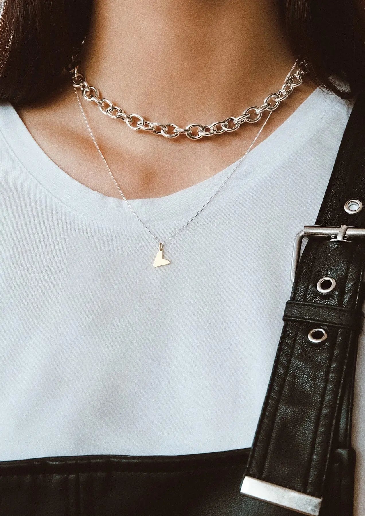 A close-up of a person wearing a Love Necklace - Gold, showcasing a sterling silver pendant with 24kt gold plating. Handmade sustainably in Lithuania and the Netherlands, measuring 8.5mm - 9.9mm wide and 8.10mm - 13mm high.