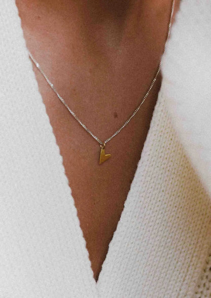 A person wearing a Love Necklace - Gold, a heart-shaped pendant on a chain. Handmade with sterling silver and 24kt gold plating, 45cm long. Sustainable packaging. Made in Lithuania and the Netherlands.