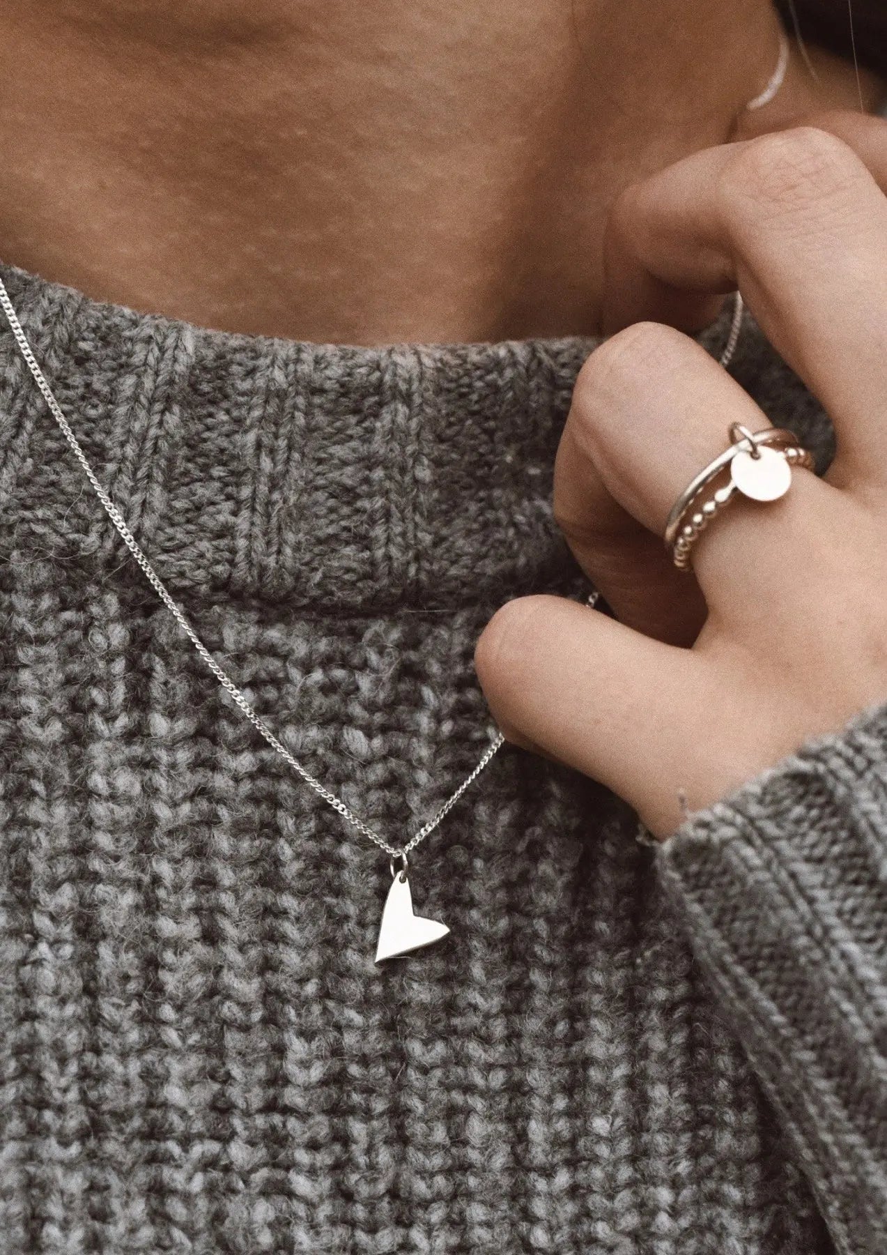 A close-up of a person wearing a Love Necklace in Sterling Silver, showcasing a heart pendant, handmade with sustainable materials, offering a two-year warranty.