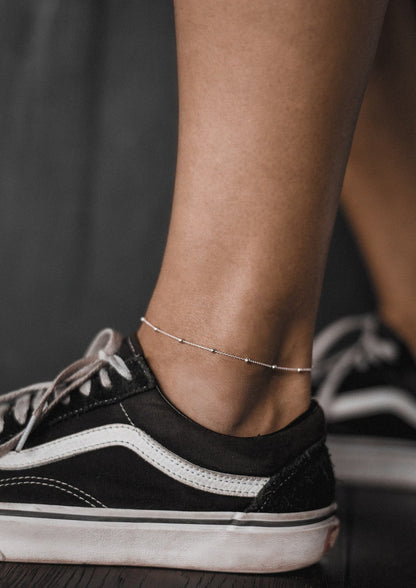 A person wearing a silver Mini Bubble Anklet on their ankle, showcasing a minimal design with silver chain and mini bubbles. Hand-made with sterling silver, adjustable chain length up to 27 cm.