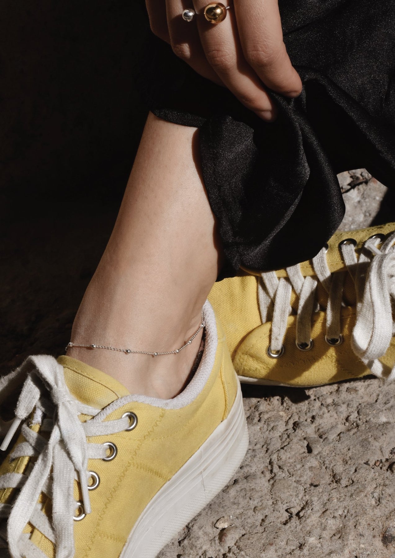 A person's ankle adorned with a silver Mini Bubble Anklet featuring delicate silver bubbles on a chain. Handmade from Sterling Silver, adjustable length, minimalist design perfect for summer.