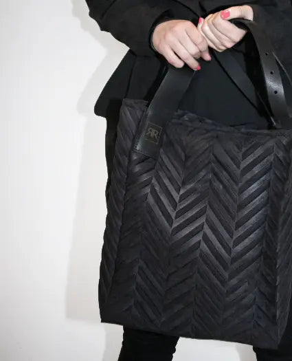 A person holding a black Mixed Material Shopper Bag in Herringbone, showcasing soft-touch fabric and genuine leather accents. Zip closure, interior pocket, and handcrafted in Europe for luxury and durability.