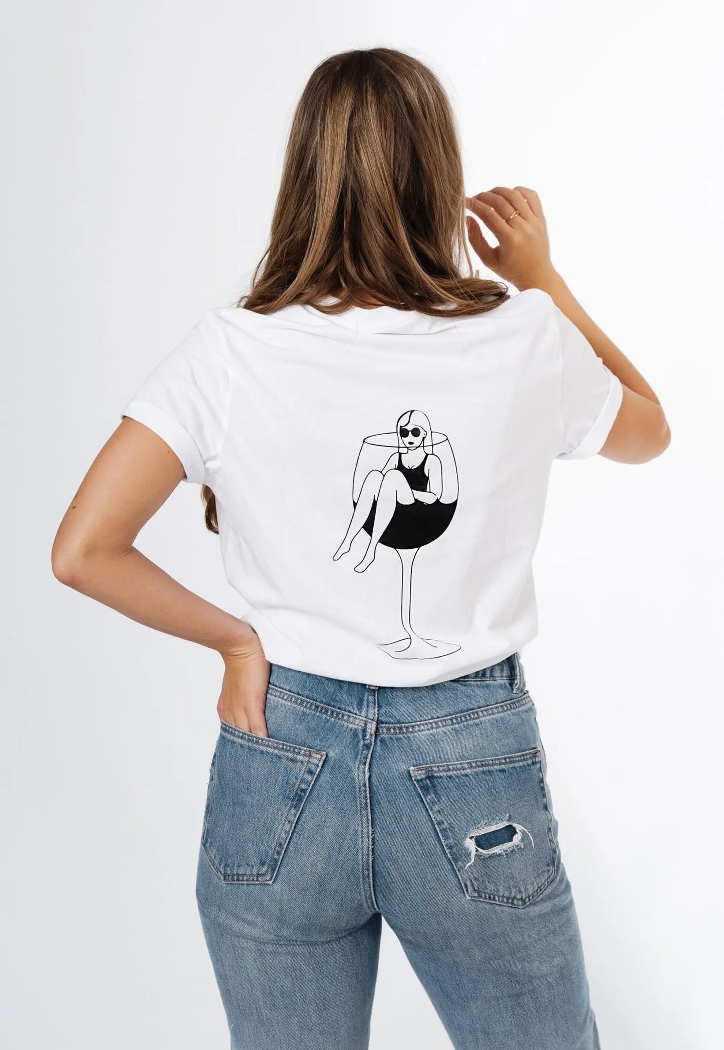 An oversized white t-shirt with a wine glass design on the back, featuring a woman sitting inside, made of organic cotton. Size chart available for XS to XL.