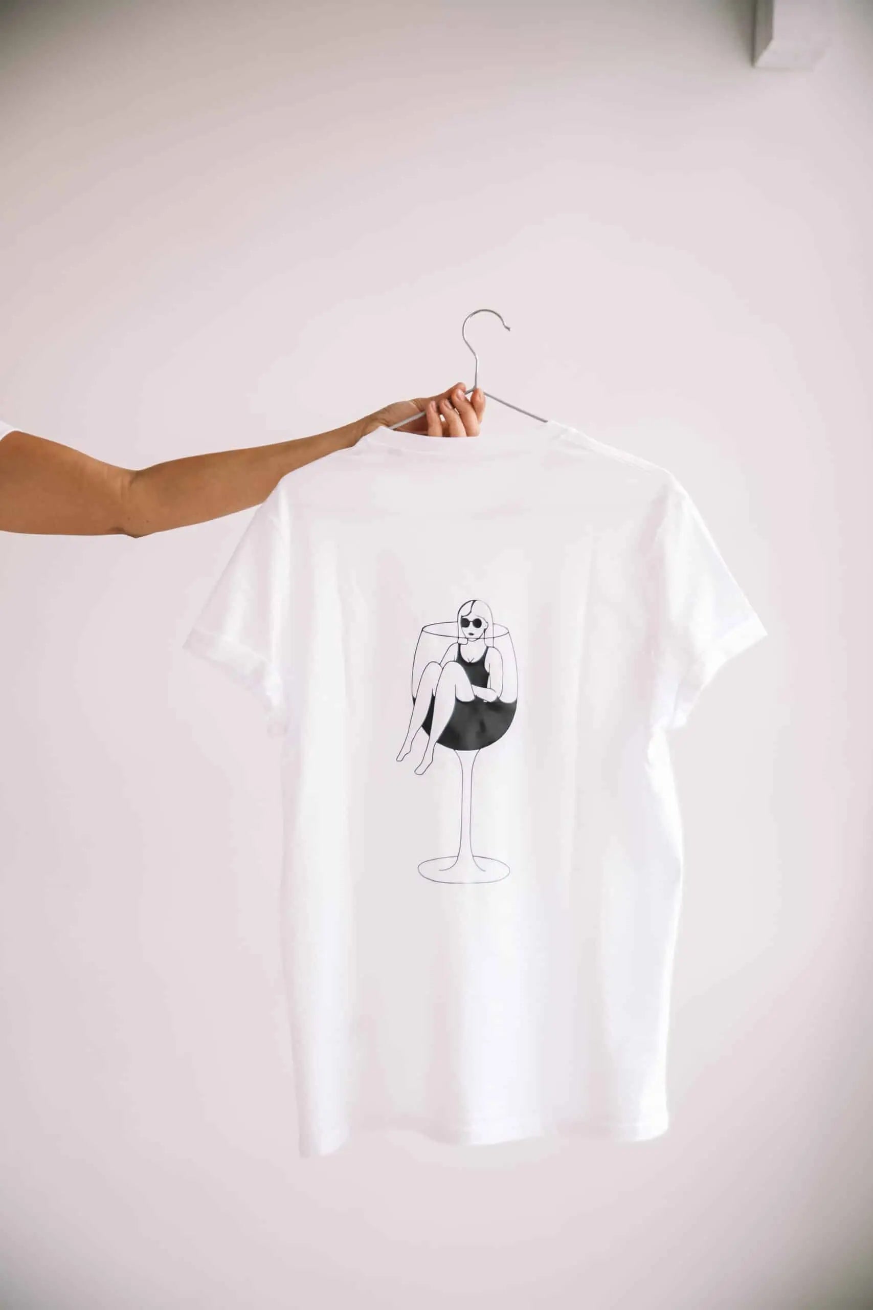 An oversized white organic cotton t-shirt featuring a drawing of a woman sitting on a wine glass. Perfect for wine lovers. Size chart available.