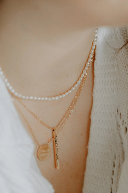 A woman wearing a freshwater pearl necklace, perfect for various occasions. Packaged in a jewelry box, this durable stainless steel piece features 2-3 mm pearls. Available in silver, rose gold, and gold.