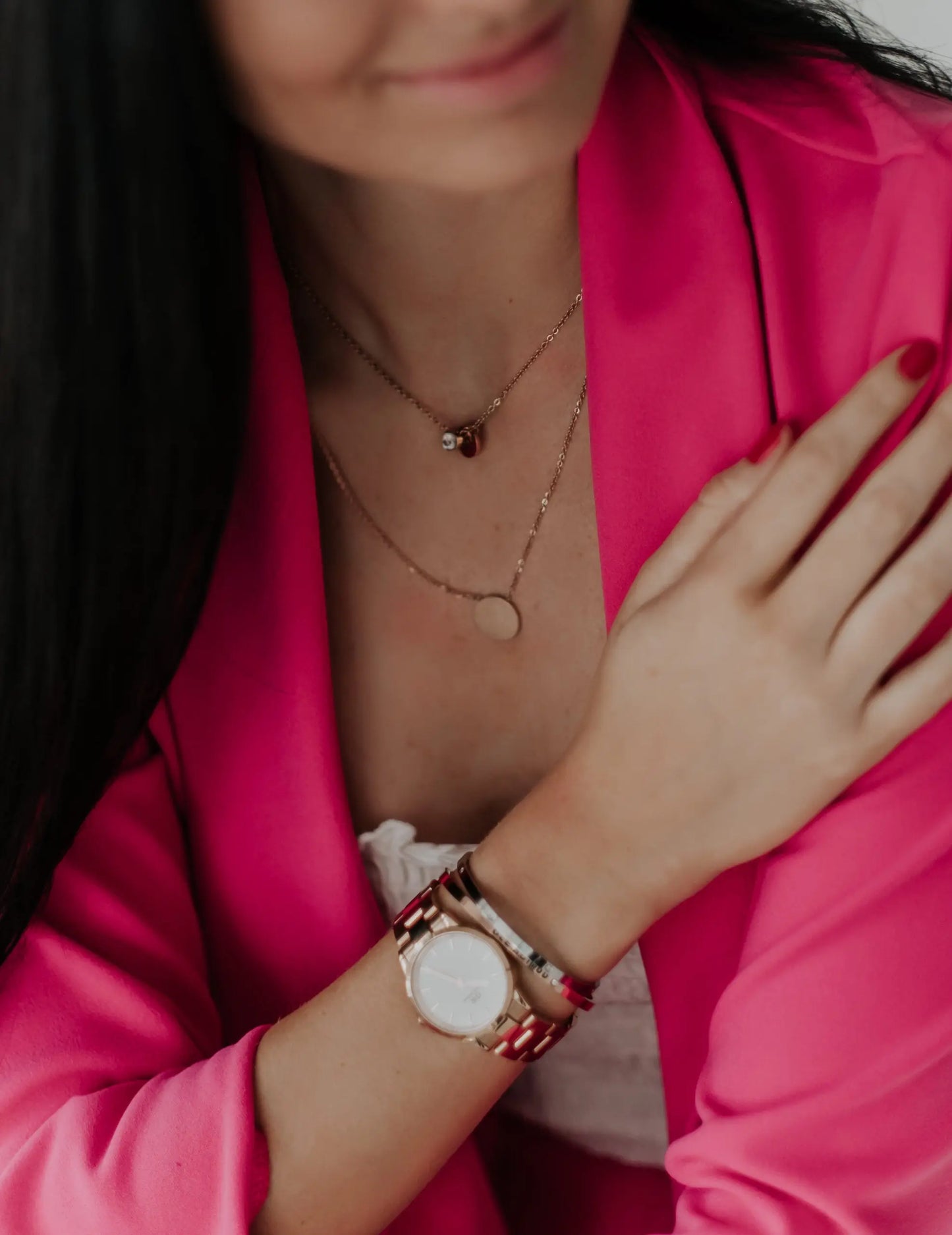 A woman in a pink jacket and gold jewelry wears the Necklace with Medallion - Good Vibes. Close-ups show a watch and necklace details. Stainless steel, 49 cm length, 18 mm medallion.