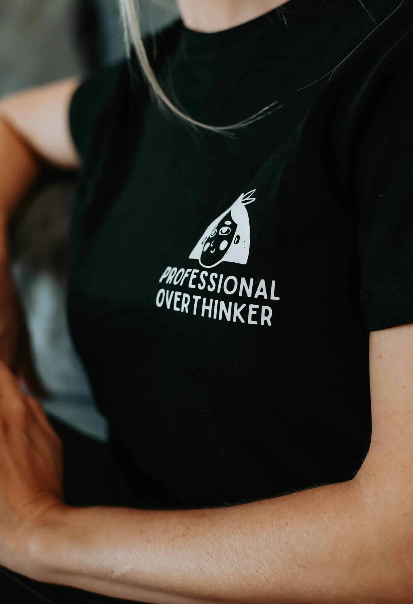 A person in a black oversized t-shirt with Professional Overthinker print, made of organic cotton. Size chart included.