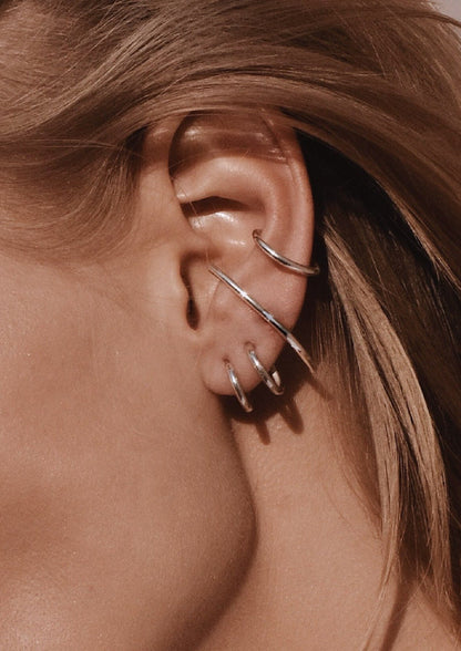 Close-up of Radius Earrings - Silver, showcasing elegant sterling silver hoops on a woman's ear. Handmade sustainably, 31.6mm length, 1.8mm thickness, with push-back clasps.