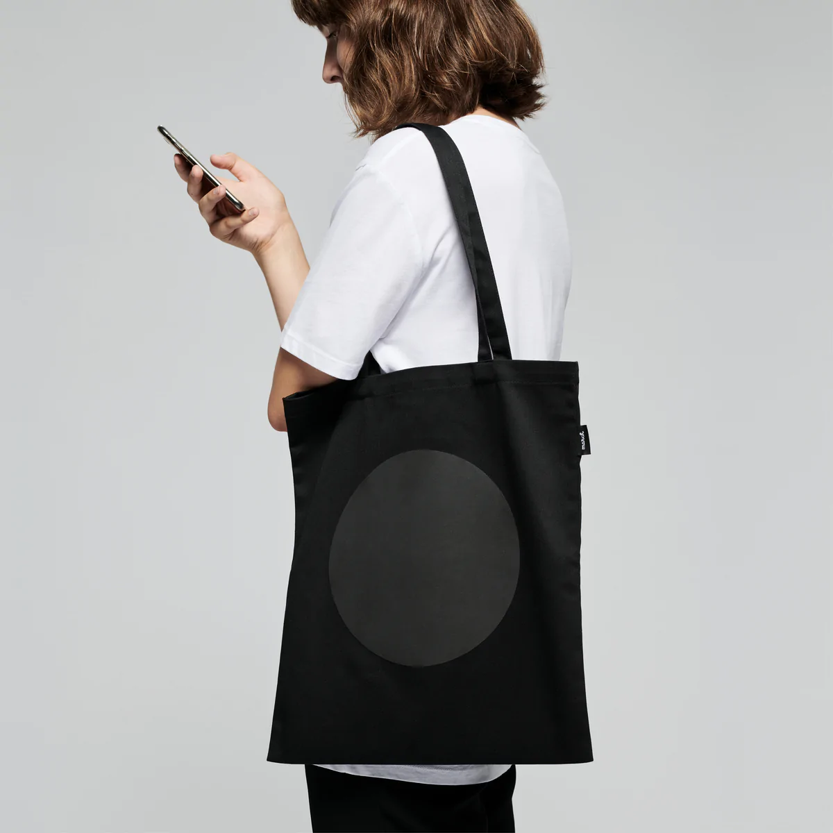 A woman holding a reflective tote DOT with a black bag. Long-lasting, reflective print & textile, inside pocket, 65% polyester, 35% cotton, OEKO-TEX® STANDARD 100. Made in Europe.