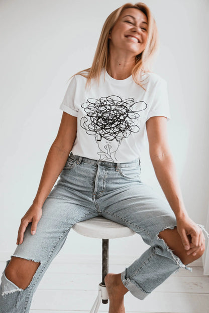 A woman in jeans sits on a stool, wearing a casual Ssshhh! T-shirt. Product features an oversize fit. Size chart: XS - XL. Washing instructions included.