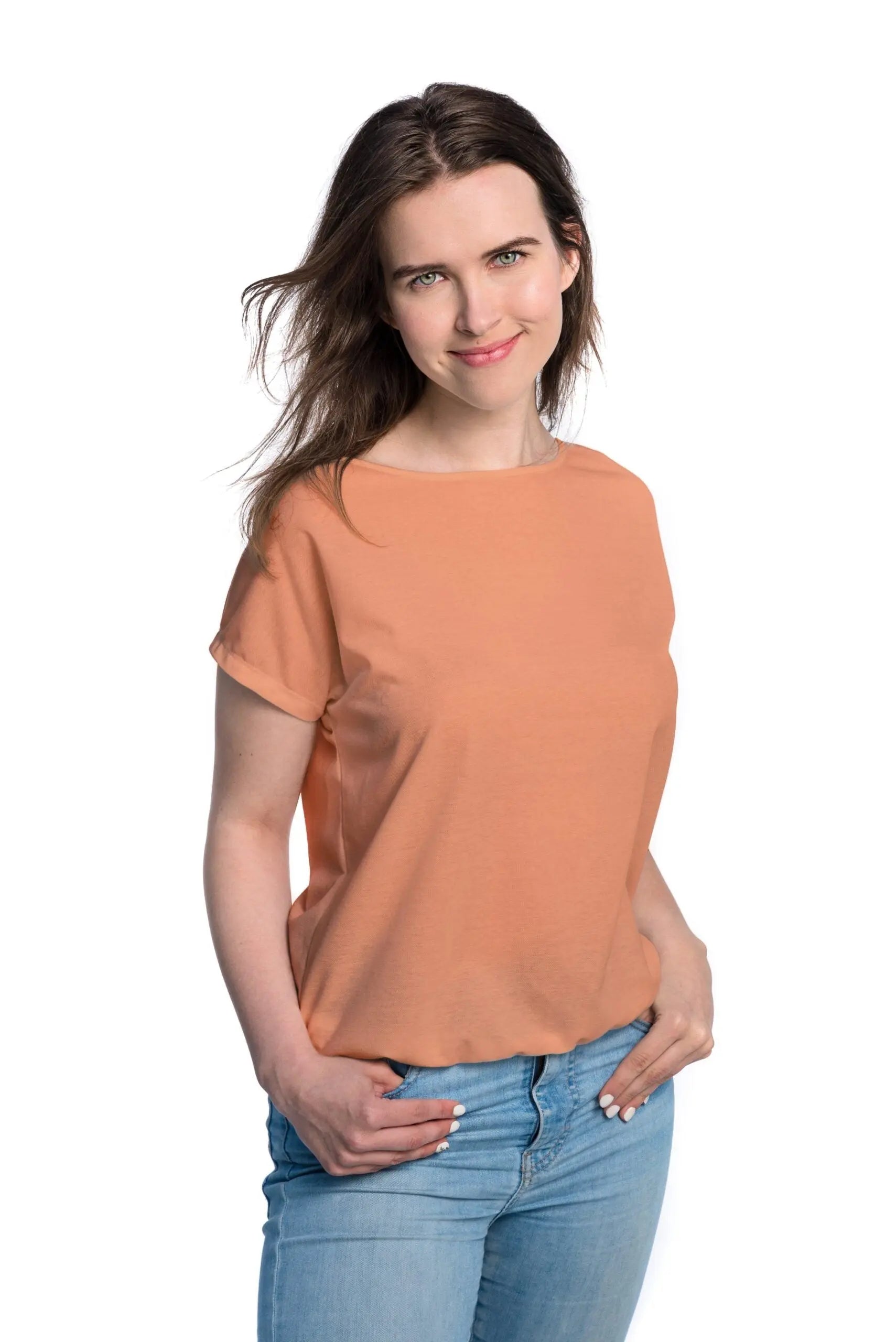 A woman in a tan-through terracotta T-shirt, hands in pockets, showcasing the spacious cut for outdoor comfort. Fabric allows healthy tanning with UVA protection. Sizes XS-XXL.