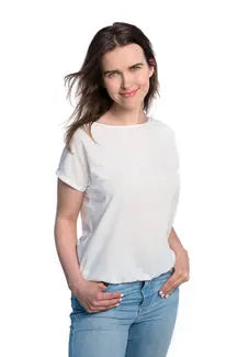 A woman in a white tan-through T-shirt, hands in pockets. Spacious cut for comfort during outdoor activities. Fabric allows healthy tanning with UVA penetration. Sizes XS-XXL available.