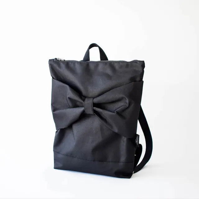 Black Bow Backpack with waterproof polyester, large bow detail. Versatile, durable, and stylish. Features adjustable straps, zipper closure, laptop pocket. Height 38 cm, width 34 cm.
