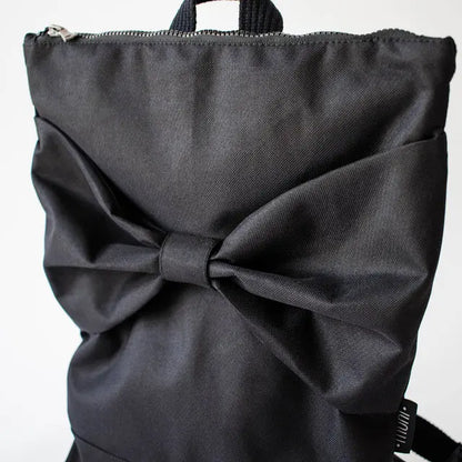 Black Bow Backpack with waterproof polyester, large bow detail. Versatile for work or play, with laptop pocket, adjustable straps, and grey lining. Dimensions: 38cm H x 34cm W.