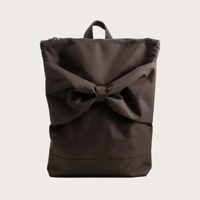 A brown waterproof MUNI backpack with a large bow detail, ideal for daily use. Features adjustable straps, zipper closure, and compartments for a 13 laptop. Dimensions: 38cm height, 34cm width.