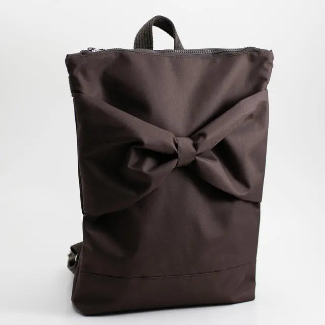 A brown waterproof MUNI backpack with a large bow detail. Roomy with adjustable straps, zipper closure, and pockets for a 13 laptop. Dimensions: 38cm height, 34cm width.