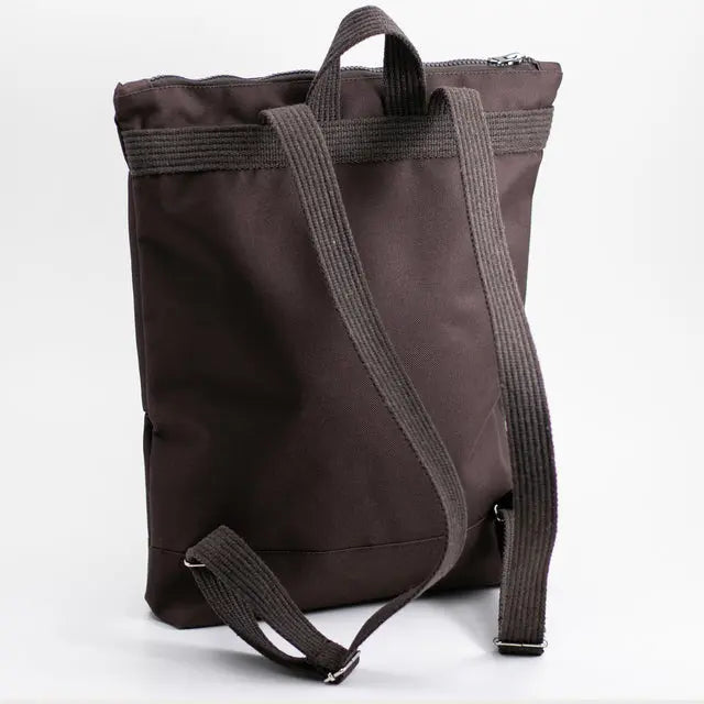 A brown waterproof MUNI backpack with a large bow detail, featuring adjustable shoulder straps, zipper closure, and pockets for a 13 laptop. Dimensions: 38cm height, 34cm width.